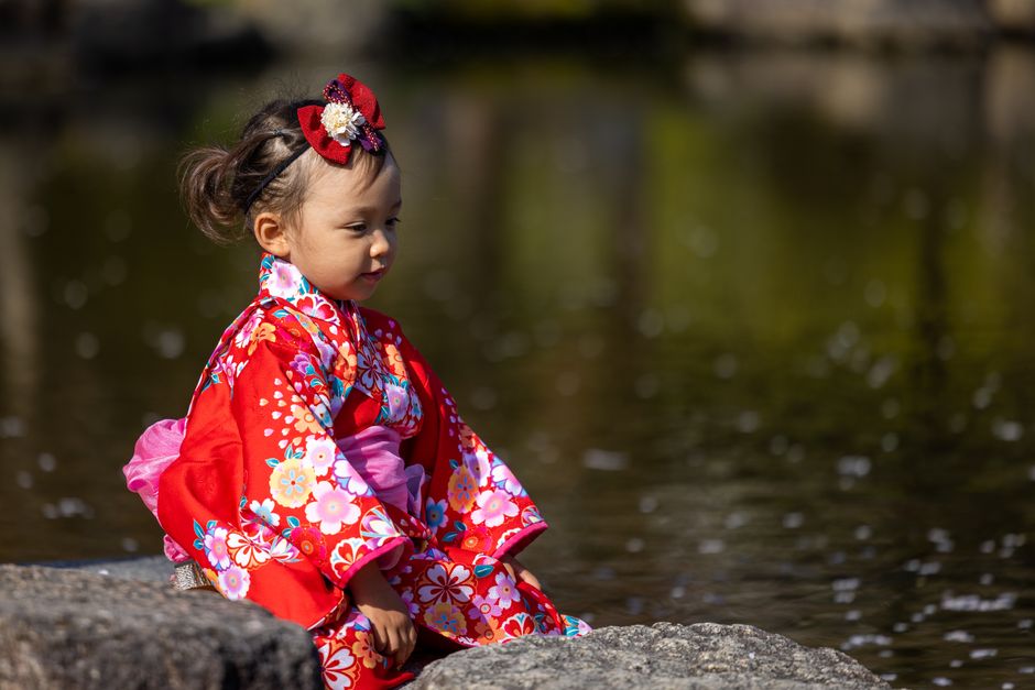 赤い着物を着た女の子が水辺の岩の上に座っている